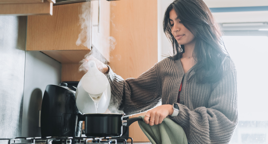student pouring water from kettle into saucepan