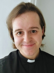 A headshot of Sam Fletcher, dressed in black with a priest